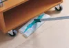 A mop is being used to clean under a wooden furniture piece with wheels. Náhľad obrázku produktu
