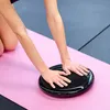 A person's hands are placed on a black balance pad on a pink yoga mat. Produktbild-Vorschau