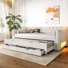 A beige daybed with a pull-out trundle bed and storage drawers, set up in a well-lit room with a plant and artwork. Voir les images du produit