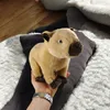 A plush capybara toy is held in a hand over a rug. Produktbild-Vorschau