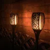 Two solar garden torches with a flame effect are lit up at night, placed in front of a wooden fence and a lattice fence. Náhled obrázku produktu