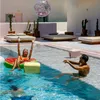 A couple enjoys a day by the pool, with one person floating on a watermelon-shaped raft and the other reaching for a glittery ball. Podgląd zdjęcia produktu