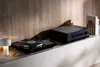 A turntable and amplifier are displayed on a shelf in a modern room with a wood-paneled wall. Produktbild-Vorschau