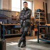 A man in workwear stands in a workshop with tools and equipment in the background. Produktbild-Vorschau