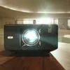 A projector is on a wooden table in a room with a person in the background. Anteprima dell’immagine prodotto