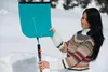 A woman is assembling a turquoise snow shovel in a snowy environment. Náhled obrázku produktu