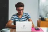 A young person is smiling while looking at a laptop. Produktbild-Vorschau