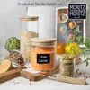 A collection of glass jars filled with various food items like lentils, grains, and herbs, arranged on a wooden cutting board with some produce and greenery in the background. Produktbild-Vorschau