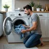 A man is kneeling and loading laundry into a washing machine. Produktbild-Vorschau