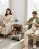 A man and a woman are sitting in chairs in a living room, each using electronic devices. Náhled obrázku produktu