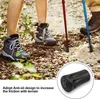 Close-up of a person's legs and feet wearing hiking boots, with two trekking poles (one red, one blue) planted in the ground. The ground is covered in leaves and dirt. A circular inset shows a black rubber tip for a trekking pole. Produktbild-Vorschau
