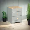 A gray bedside table with a wooden top and three drawers, placed on a wooden floor next to a potted plant and a fern. Anteprima dell’immagine prodotto