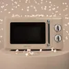 A retro-style beige microwave oven is placed on a display stand, surrounded by scattered popcorn. Produktbild-Vorschau