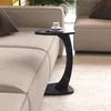 A black marble-look C-shaped side table with a white cup and saucer on it, placed next to a beige sofa.