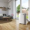 A portable air conditioner is shown in a living room next to a sliding glass door leading to a backyard. Voir les images du produit