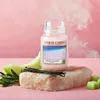 A Yankee Candle 'Pink Sands' jar candle is displayed on a pink background, surrounded by decorative elements like melon slices, vanilla beans, and greenery. Podgląd zdjęcia produktu