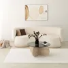 A modern living room scene with a fluffy white couch, a glass-top coffee table, and abstract art on the wall. Produktbild-Vorschau