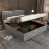 A bed with its storage compartment open, revealing stored items. The bed is in a room with wooden walls and curtains. Náhľad obrázku produktu