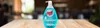 A bottle of dish soap sits on a wooden table in front of a blurred background. Produktbild-Vorschau