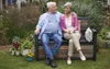 An elderly couple sitting on a garden bench in a garden setting. Produktbild-Vorschau