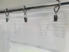 A close-up view of a white sheer curtain hanging from a metal rod with clip rings. Produktbild-Vorschau
