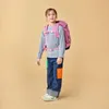 A young girl wearing a backpack and jeans stands against a plain background. Náhled obrázku produktu