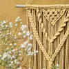 A close-up of a yellow macrame wall hanging with small white flowers in the foreground. Podgląd zdjęcia produktu