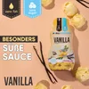A bottle of vanilla-flavored sweet sauce is displayed on a peach-colored background, surrounded by scoops of ice cream and vanilla beans. Produktbild-Vorschau