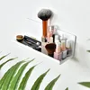 A white shelf mounted on a white wall, holding various makeup items and brushes. Green leaves are in the foreground. Voir les images du produit
