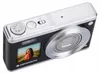 A compact digital camera is shown from a slightly elevated angle against a white background. The camera is black with silver accents and features a lens, a small screen displaying a photo of a woman, and various buttons and a dial on the top. The brand nam Náhľad obrázku produktu