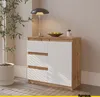 A modern sideboard with white drawers and a wood-tone frame, placed in a room with a plant and a lamp. Voir les images du produit