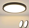 A close-up shot of a modern LED ceiling light fixture with a dark frame and a bright white diffuser, mounted on a white ceiling. Two smaller, similar lights are visible in the lower right corner. Produktbild-Vorschau