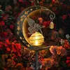 A solar garden light shaped like a crescent moon with a fairy and a lantern, set amongst red and orange flowers. Produktbild-Vorschau