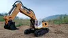A remote-controlled excavator is placed on a dirt ground with a hilly, vegetated background under a cloudy sky. Náhľad obrázku produktu