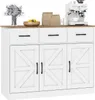 A white sideboard with a wooden top, featuring three drawers and three cabinet doors with a barn door design. It is decorated with a vase of flowers, a bowl of lemons, and two paper bags on top, along with a white espresso machine. Náhľad obrázku produktu