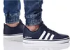 A person wearing dark blue Adidas sneakers and denim jeans. Náhľad obrázku produktu