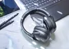 A pair of black headphones rests on a desk next to a laptop and pens. Anteprima dell’immagine prodotto