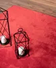 A red rug with two black lanterns and white candles on it, with a wooden floor in the background. Produktbild-Vorschau