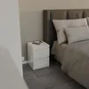 A white nightstand with two drawers is placed next to a bed in a bedroom. Voir les images du produit