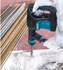 A person wearing white gloves is using a Makita demolition hammer to break up concrete. A pile of rebar is visible in the background. Anteprima dell’immagine prodotto
