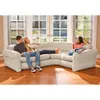 Three people relaxing on an inflatable sectional sofa in a living room with large windows. Produktbild-Vorschau