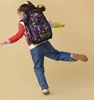 A young girl is shown from behind, wearing a backpack and jeans, with her arms outstretched as if dancing or playing. Náhľad obrázku produktu