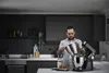 A man is in a modern kitchen, preparing to add ingredients to a stand mixer. Voir les images du produit
