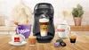 A coffee machine with various coffee cups and coffee pods arranged on a wooden surface. Produktbild-Vorschau
