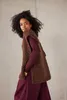 A woman is posing in a studio setting, wearing a brown knitted vest over a maroon long-sleeved shirt and maroon wide-leg pants. Produktbild-Vorschau