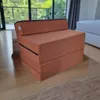 A folded mattress/chair in a room with a window and a bed in the background. Náhľad obrázku produktu