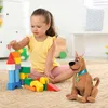 A young girl plays with building blocks next to a Scooby-Doo plush toy in a room. Náhled obrázku produktu
