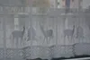 A white lace curtain with a deer and Christmas tree pattern, seen through a window. Produktbild-Vorschau