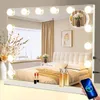 A vanity mirror with lights is placed on a dresser in front of a bed, with makeup and decorative items around it. Produktbild-Vorschau