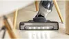 A close-up shot of a cordless vacuum cleaner head with LED lights on a wooden floor. Produktbild-Vorschau